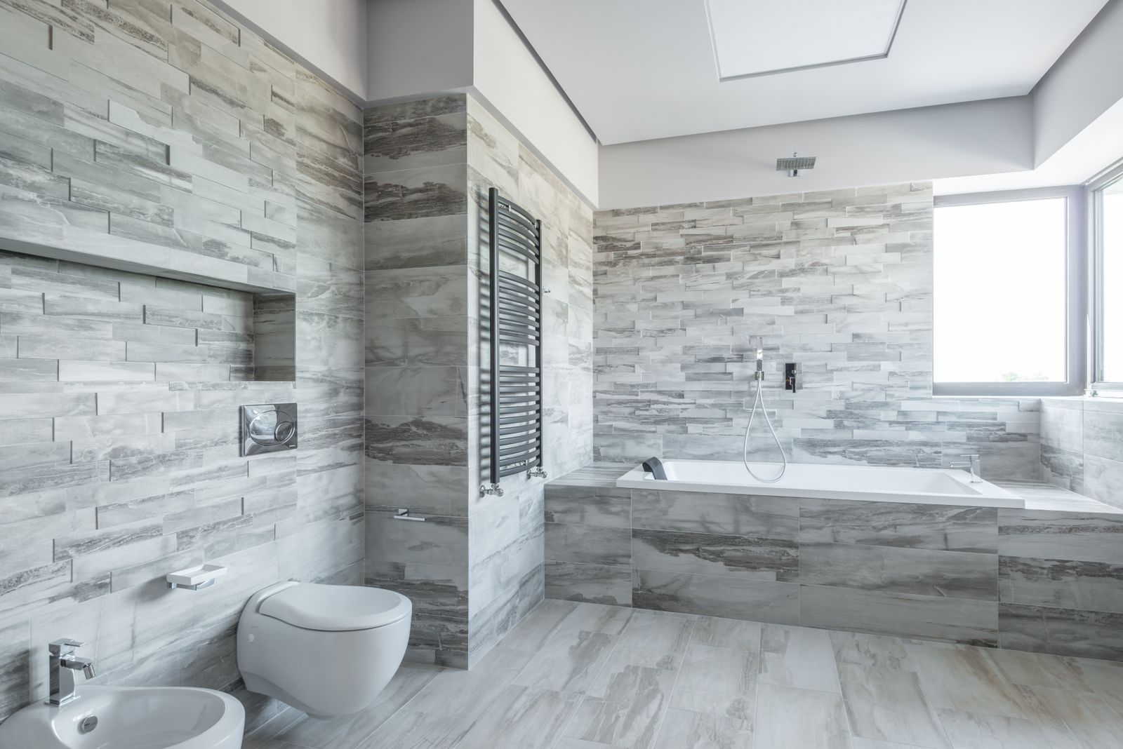 Baño con alicatado gris, bañera, inodoro y toallero.